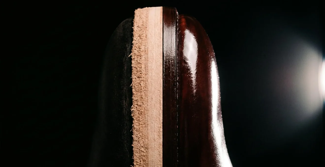 Comparaison en split-screen vertical d'une tranche de semelle : côté gauche brut et mat en cuir naturel, côté droit poli avec finition cirée effet miroir acajou sur fond noir