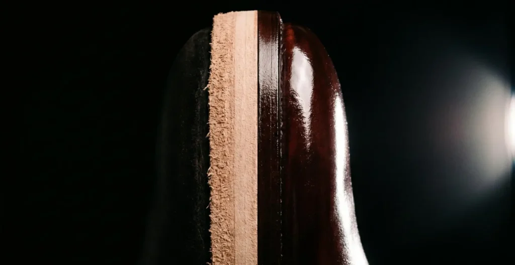 Comparaison en split-screen vertical d'une tranche de semelle : côté gauche brut et mat en cuir naturel, côté droit poli avec finition cirée effet miroir acajou sur fond noir Comparaison en split-screen vertical d'une tranche de semelle : côté gauche brut et mat en cuir naturel, côté droit poli avec finition cirée effet miroir acajou sur fond noir